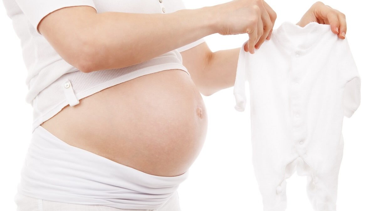 Mulher grávida com roupinha de bebê em mãos